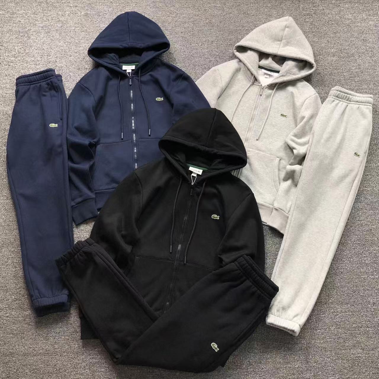 Three tracksuits in black, blue, and gray on a gray surface